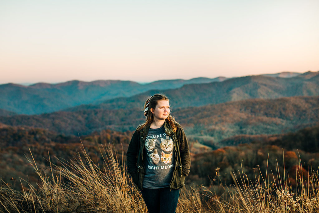 a girl wearing a t-shirt and green jacket looking off into the distance with the blue ridge mountains in the distance, the t-shirt has cats on it and says "I'm feeling great right meow"